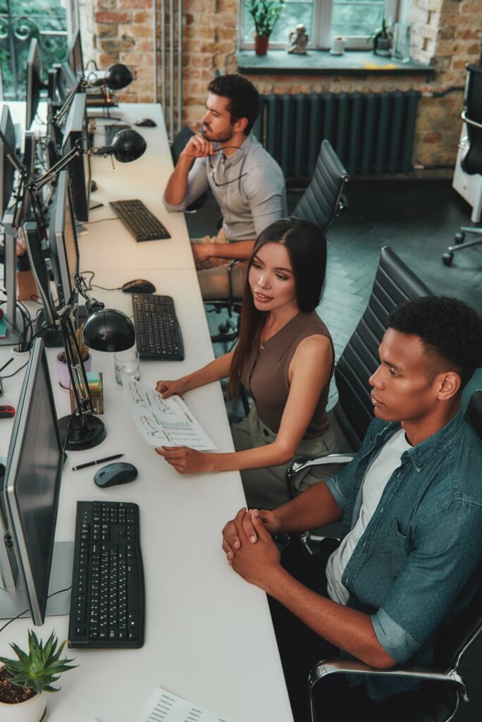 Top view of multiethnic team working on computers and talking with each other while sitting in